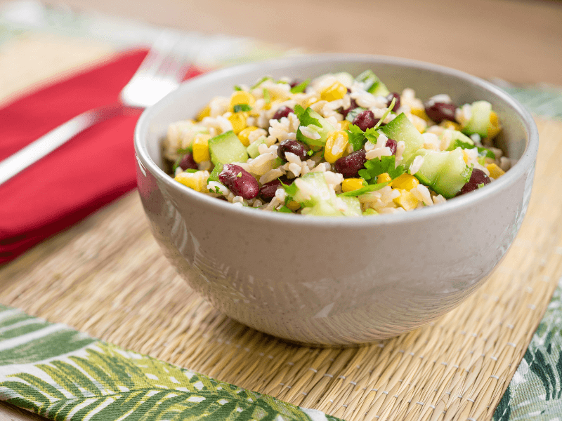 Brown rice and bean salad with cucumber, sweetcorn, kidney beans, and herbs tossed in a zesty lime‑cumin dressing, served in a speckled bowl.