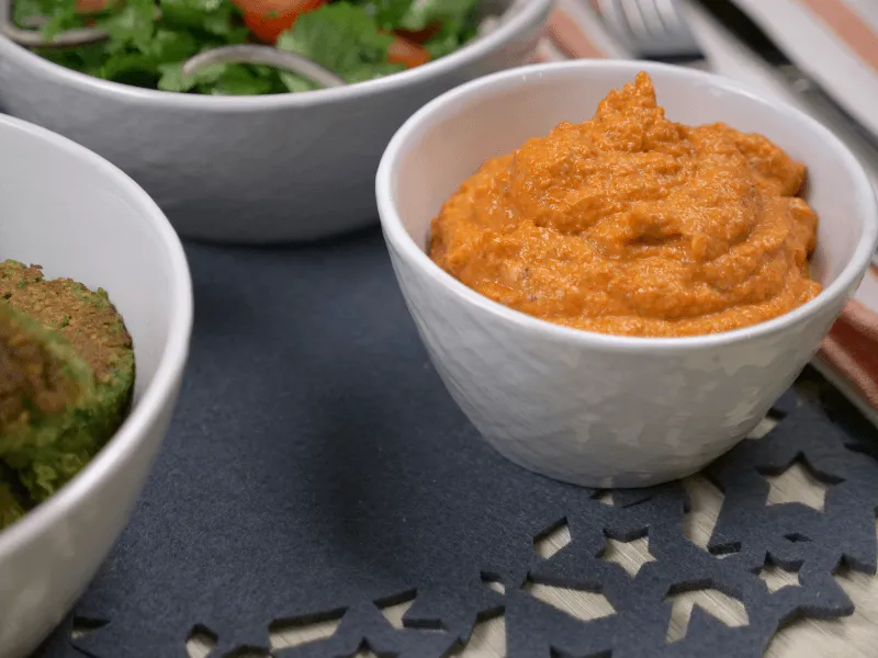 Roasted red capsicum spread (muhammara) — a Middle Eastern dip of roasted red peppers blended with walnuts, breadcrumbs, olive oil, and pomegranate molasses, served in a white bowl.