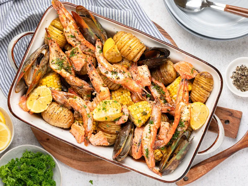 Seafood tray bake with prawns mussels salmon corn and hasselback potatoes in roasting pan, easy summer seafood dinner with lemon and herbs, dairy free gluten free family friendly meal