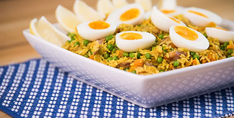 Smoked fish and pea kedgeree—curried rice with peas topped with soft‑boiled egg halves and lemon wedges in a white serving dish.