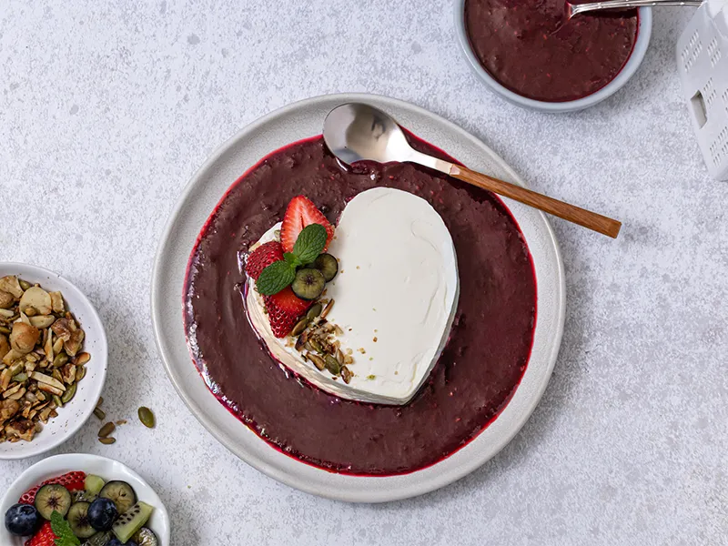 Heart-shaped strained yoghurt Coeur à la crème dessert on berry coulis, garnished with fresh strawberries, kiwi, mint and toasted nuts on a white plate, overhead view, gourmet gluten free summer dessert presentation.
