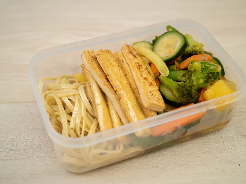 Sweet and sour vegetables with tofu strips and noodles in a lunch box.