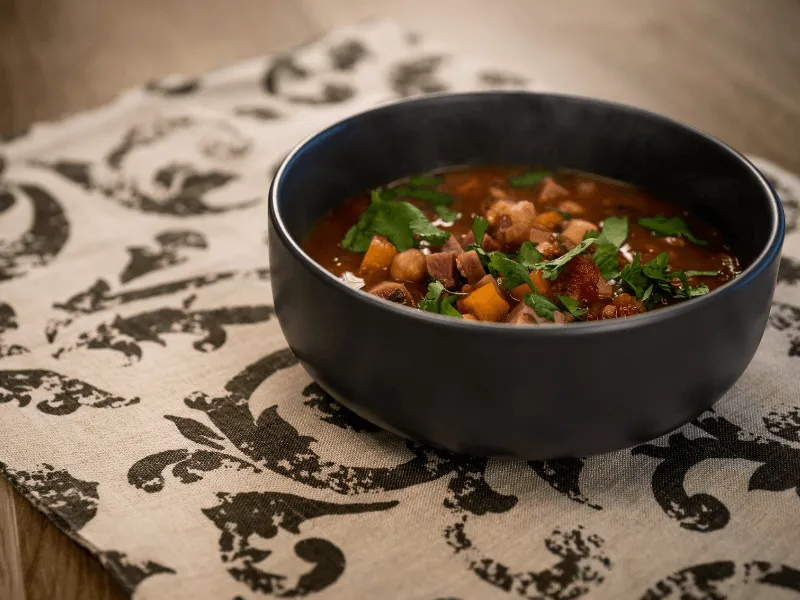 Tomato, chickpea, and peanut soup with herbs in a black bowl, inspired by West African peanut stew with a creamy tomato‑peanut base.