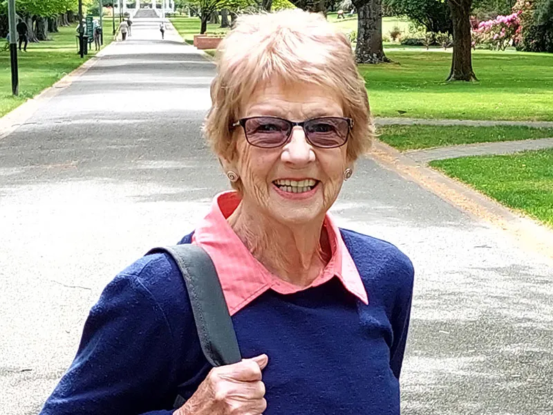 Photo of Clodagh, an 80-year-old volunteer for the Heart Foundation's annual street collection Big Heart Appeal. She is wearing sunglasses, a pink shirt and a blue jumper. She is smiling into the camera.