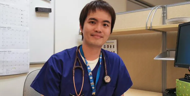 Dr Bernard Wong sitting at his desk wearing hospital scrubs