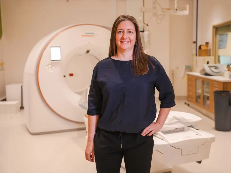 Dr Charlotte Greer standing beside a photon-counting CT scanner used for advanced heart imaging research in Christchurch.