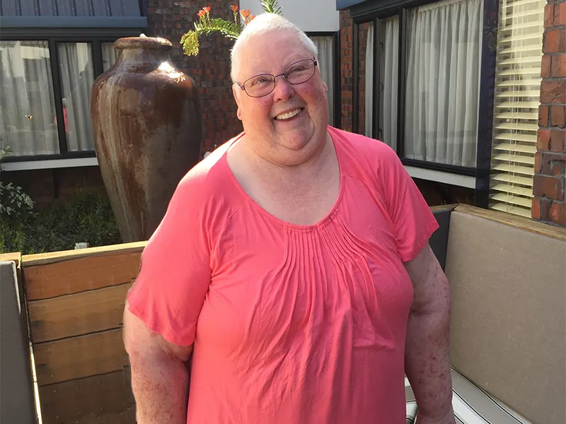 Picture of Jenny Goss standing in her back garden. She wears a pink t-shirt and black pants.