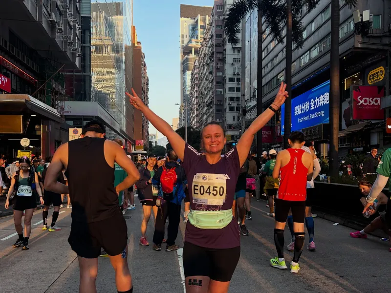 Marathon runner raising arms in celebration on a city street surrounded by other race participants.