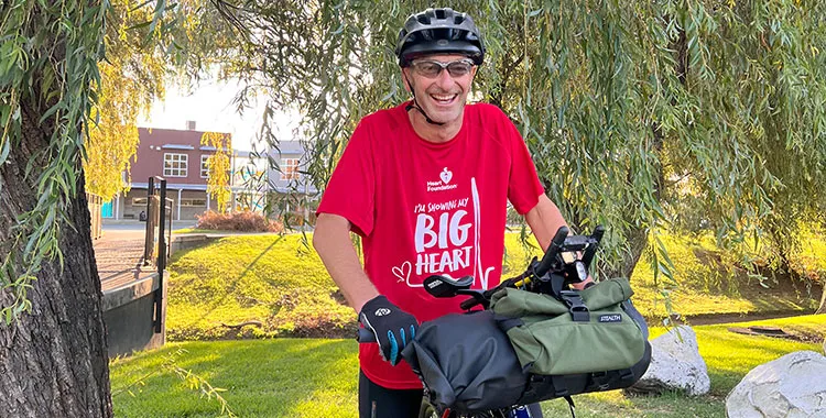 A picture of Dr Nigel Level astride his bike, wearing a red Heart Foundation t-shirt and a cycling helmet