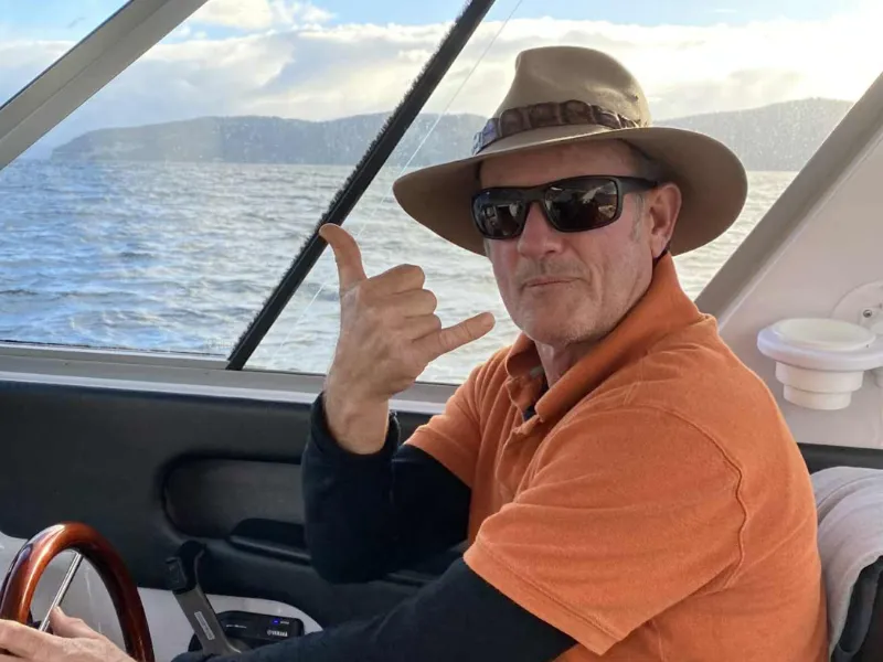 Middle‑aged man in orange shirt steering a boat in New Zealand, enjoying an active outdoor lifestyle on the water