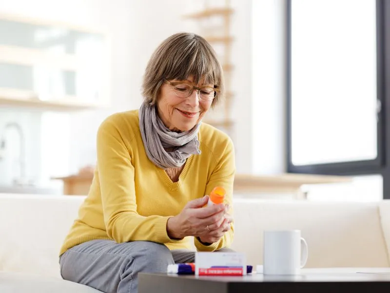 Woman sitting on a couch reading the label on a medication container.