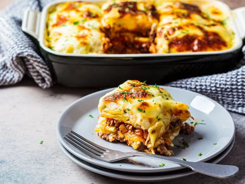 Vegetarian moussaka dish topped with golden cheese and fresh herbs on a gray plate.