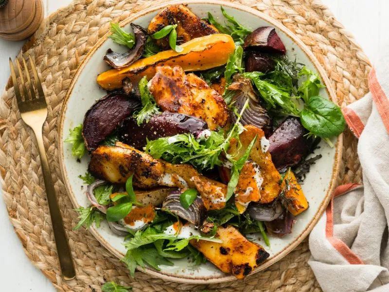 Warm roasted butternut and halloumi salad served with sundried tomato yoghurt and fresh basil on a beige plate