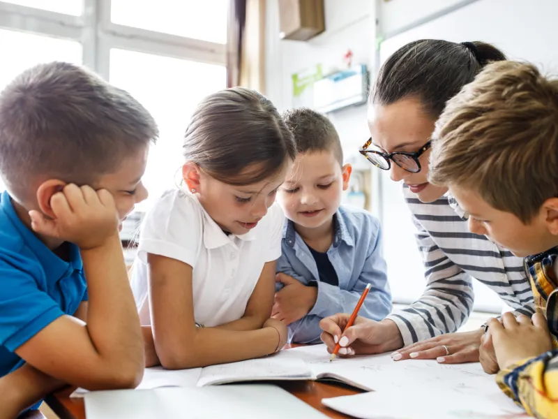 Group of primary school kids huddled together in class with their teacher engaged in discussion.