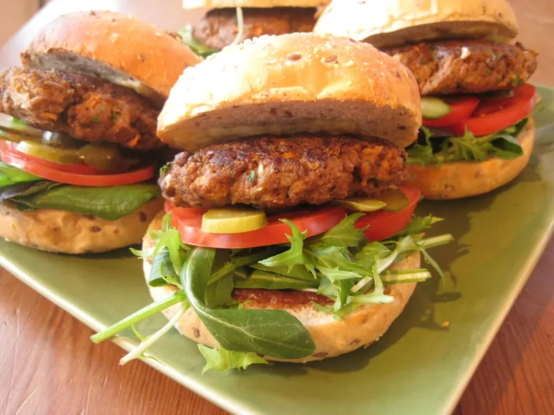 Homemade veggie burgers with wholegrain buns, fresh greens, tomato, cucumber, and pickles, served on a green plate for a healthy school lunch or snack.