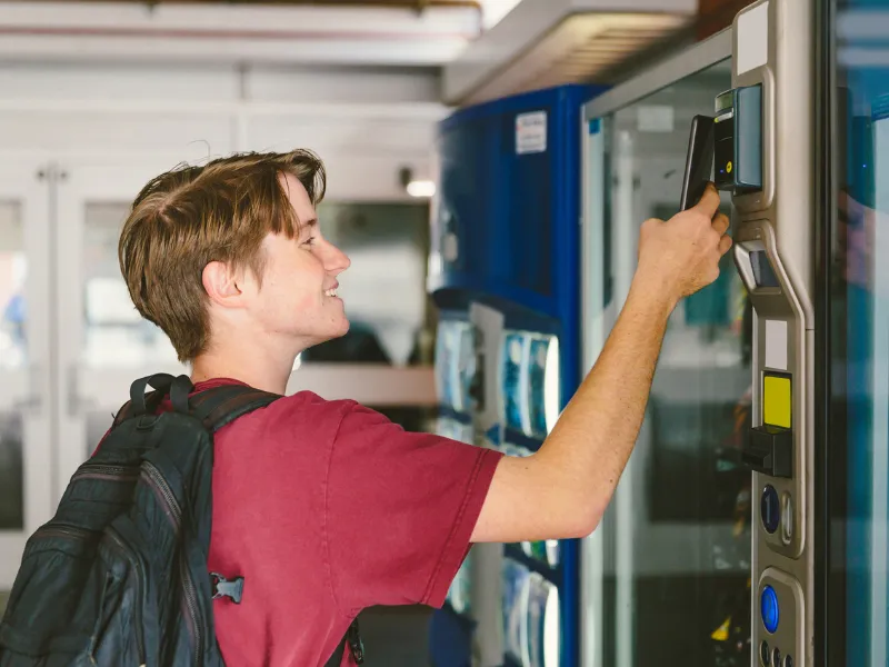 Student using contactless payment to buy snacks or drinks from a school vending machine, promoting healthy options and convenience.