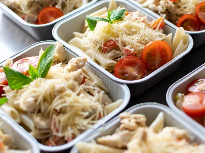 Healthy meal prep containers filled with penne pasta, grilled chicken, red bell peppers, and shredded cheese, arranged for convenient school or work lunches.