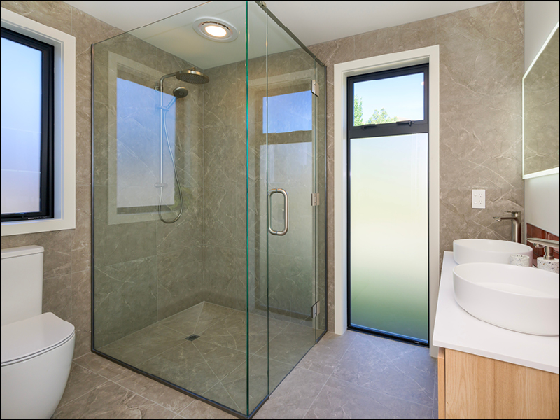 Contemporary bathroom featuring a frameless glass shower, double vanity, and frosted windows in a Wanaka house