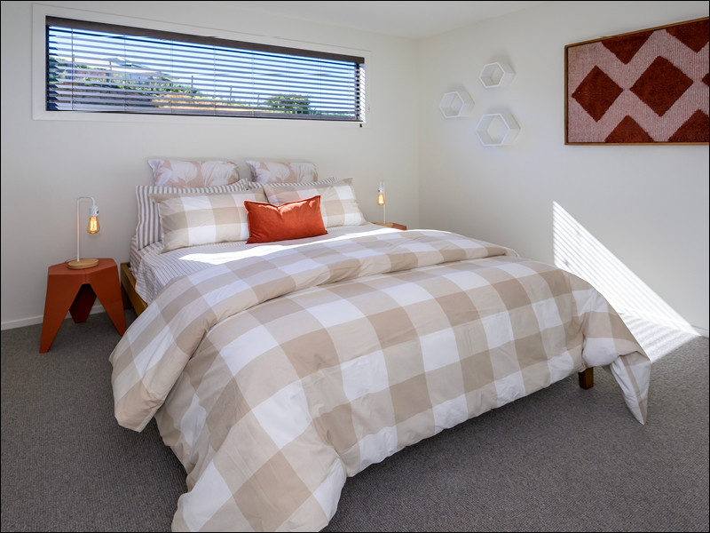 Bright guest bedroom with large window, checkered bedding, and modern decor in a Wanaka home
