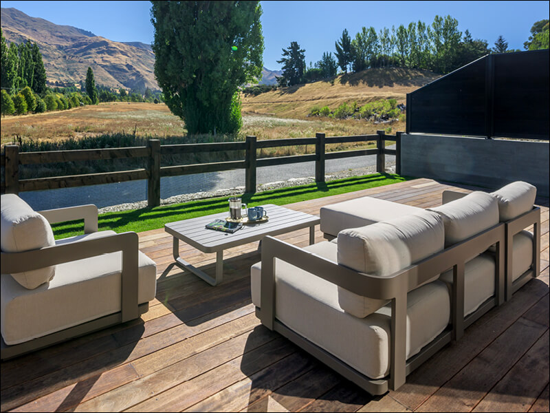 Outdoor deck with comfortable lounge seating and coffee table, overlooking scenic countryside and mountains in Wanaka.