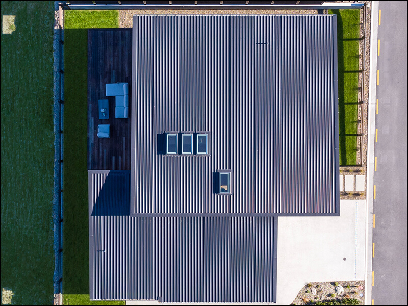 Aerial view of a contemporary Wanaka house with a dark metal roof, skylights, and spacious outdoor deck.