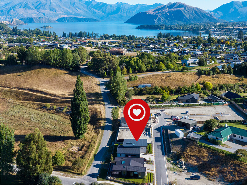 Aerial view of a residential property in Wanaka with a location pin, overlooking Lake Wanaka, surrounding houses, and scenic mountain landscape
