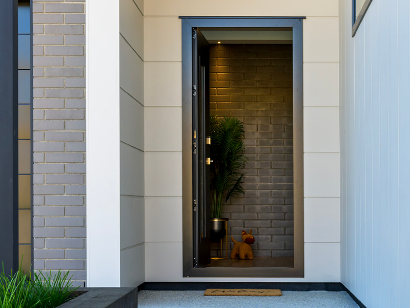Stylish front entrance of a modern Wanaka home with brick feature wall, potted plant, and welcoming decor.