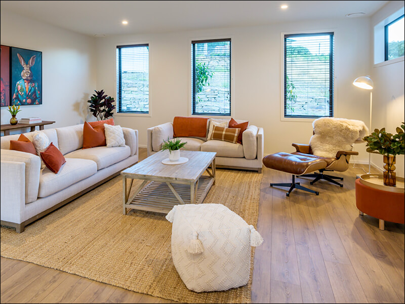 Stylish living room in a Wanaka home with neutral sofas, orange accents, Eames lounge chair, and natural light from multiple windows