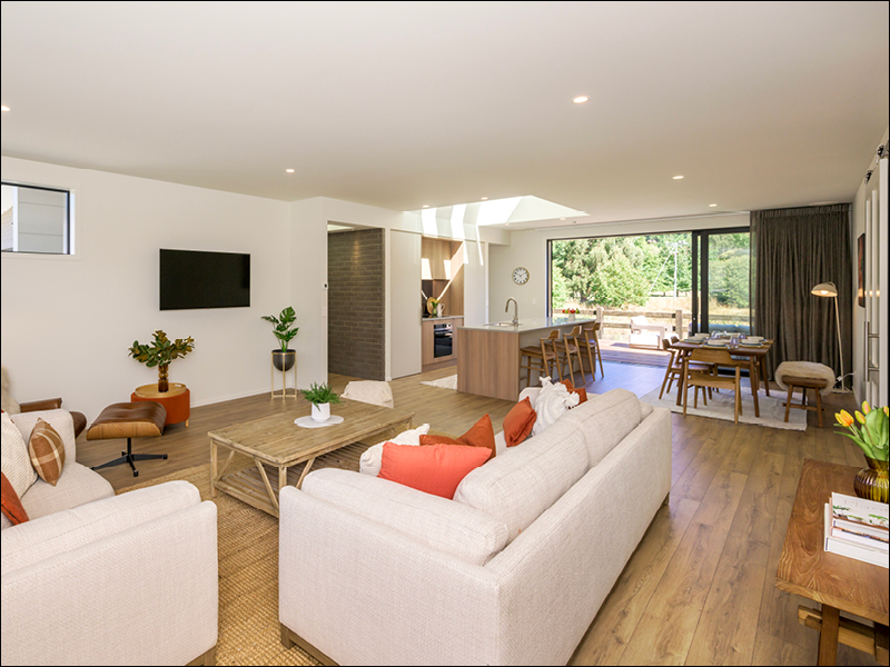 Spacious open-plan living area in a Wanaka house, showing lounge, kitchen, and dining spaces with modern furnishings and large sliding doors to the outdoors