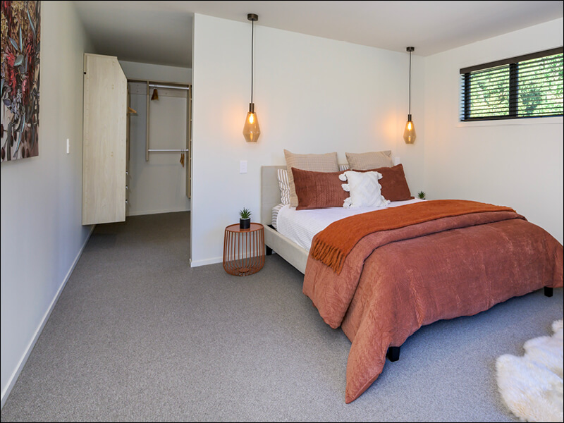 Modern bedroom in Wanaka home with warm earth-toned bedding, pendant lighting, and walk-in wardrobe