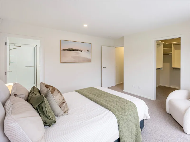 Spacious bedroom with neutral decor, green throw, walk-in closet, and ensuite bathroom in a new home.