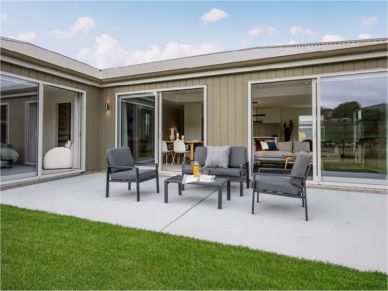 Outdoor patio with modern lounge chairs set against large sliding doors opening to living and dining areas.