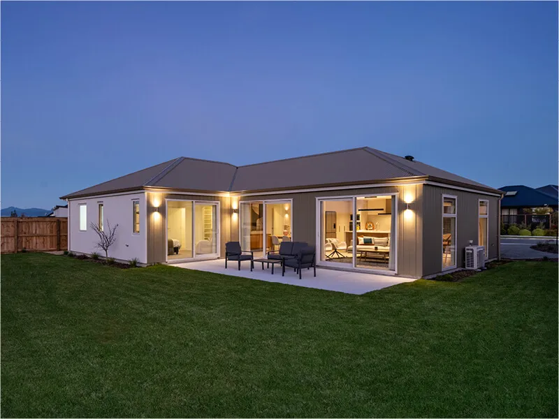 Contemporary house exterior at dusk with illuminated patio and large sliding glass doors.
