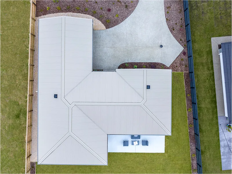 Overhead drone shot showing roof layout, driveway, yard, and outdoor patio of modern home.