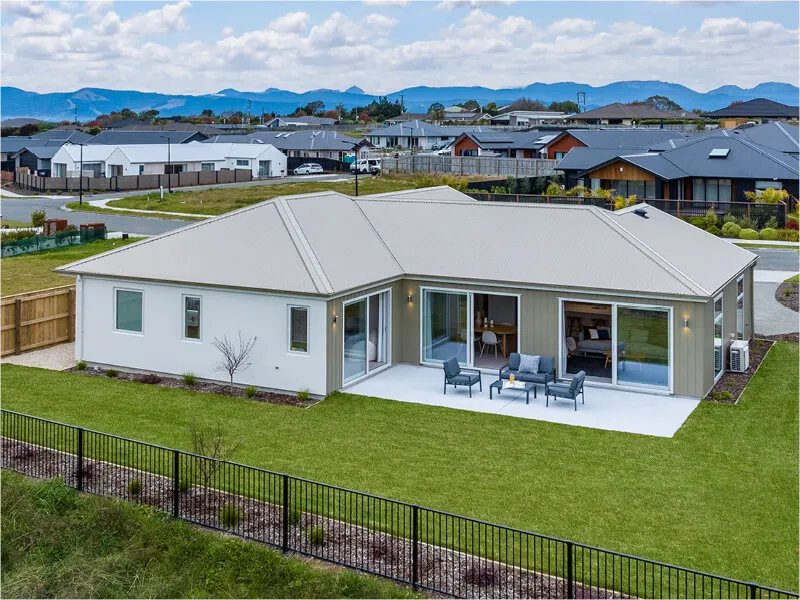 Aerial view of modern home with landscaped backyard and patio, surrounded by suburban neighborhood.