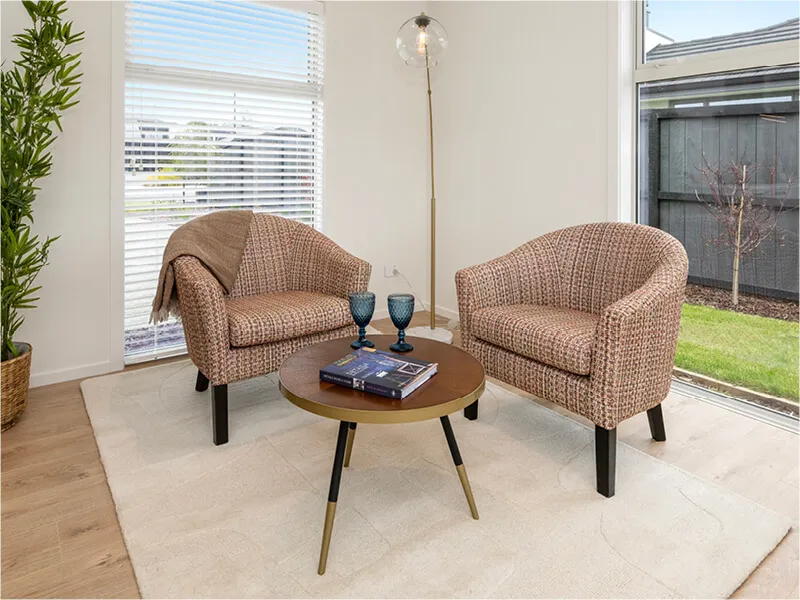 Bright living room with two patterned chairs, round coffee table, and floor-to-ceiling windows in a modern home interior.