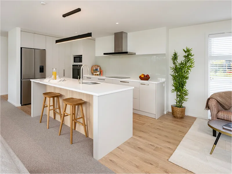 Contemporary kitchen with island seating, white countertops, and stainless steel appliances in an open-plan home.