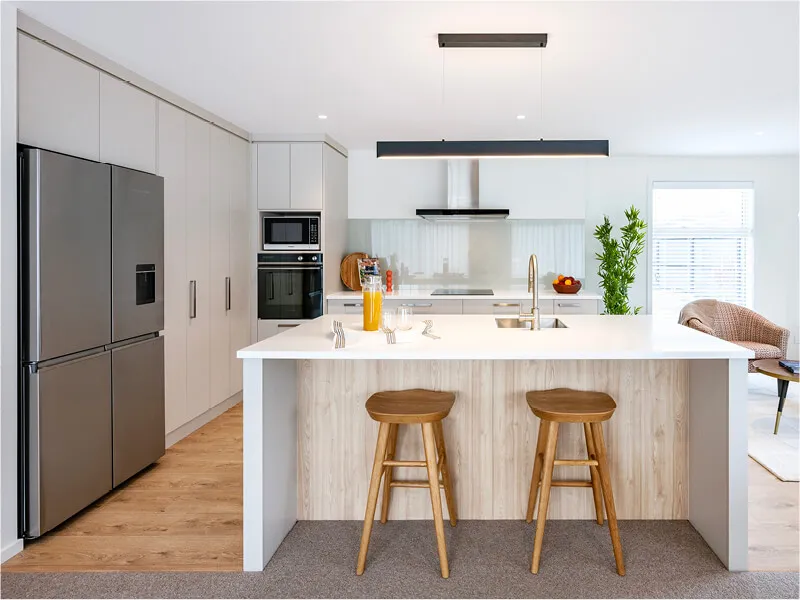 Modern kitchen with large refrigerator, built-in oven, minimalist cabinets, and a central island with wooden stools.