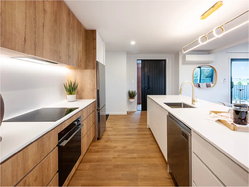Dining area of the Napier home with light wood table, transparent chairs, and adjoining modern kitchen with island bench and feature lighting.