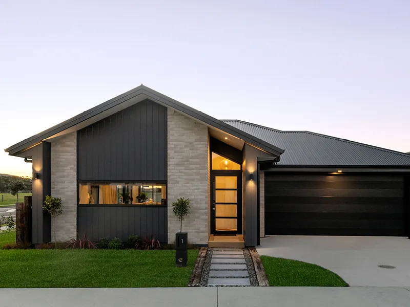 Modern Papamoa house exterior at dusk with black cladding and brick facade, lit front entry and double garage