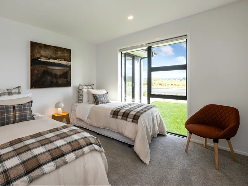 Twin bedroom with two single beds, plaid bedding and large window, modern chair and natural light.