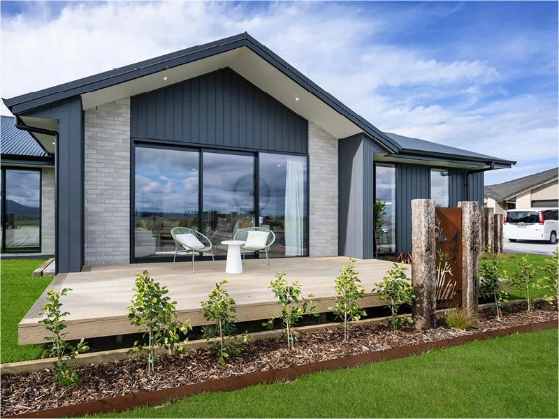 Modern rear exterior of Papamoa home with timber deck, sliding glass doors, outdoor chairs and landscaped garden.