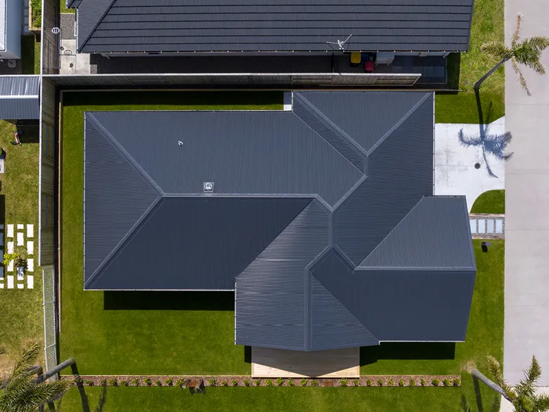 Drone aerial view of Papamoa home showing dark roof layout, backyard lawn, deck area and driveway.