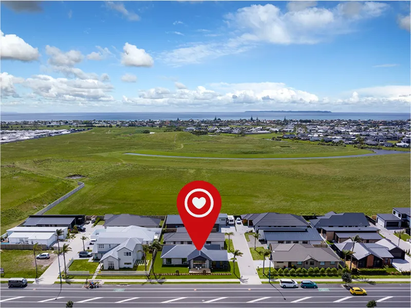 Drone view of Papamoa neighbourhood with home location pin, nearby green reserve and ocean on the horizon.