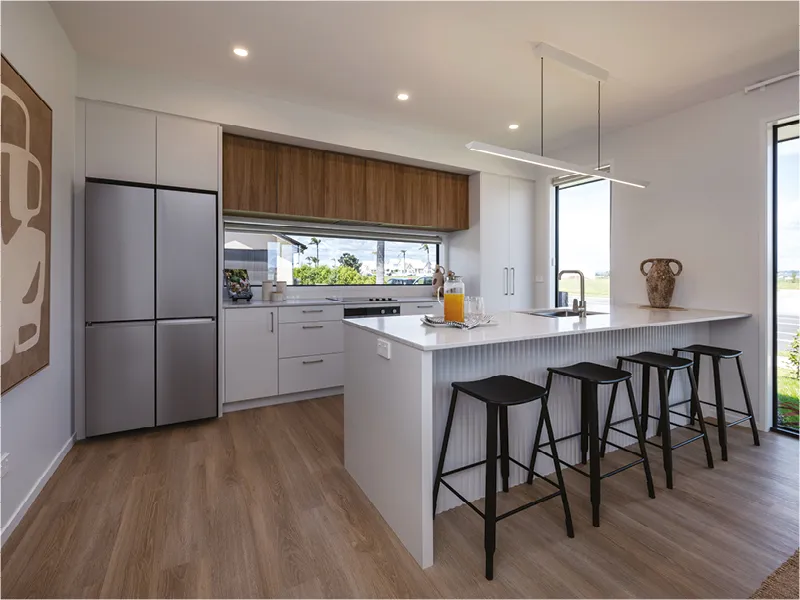 Kitchen with large white breakfast bar, black bar stools, timber splashback and modern pendant lighting.