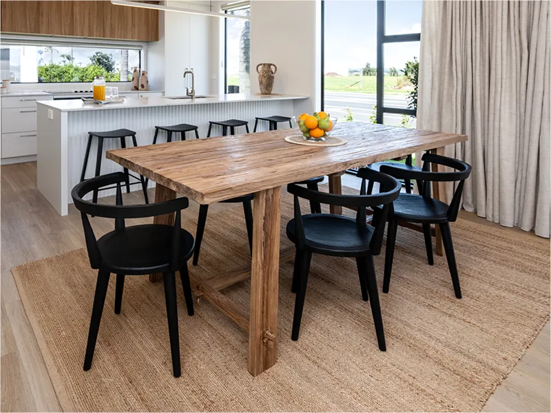 Dining area with rustic timber table and black chairs beside kitchen island and floor-to-ceiling curtains