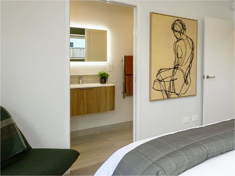 Modern bathroom vanity with timber cabinet, LED backlit mirror and towel rail, viewed from bedroom doorway