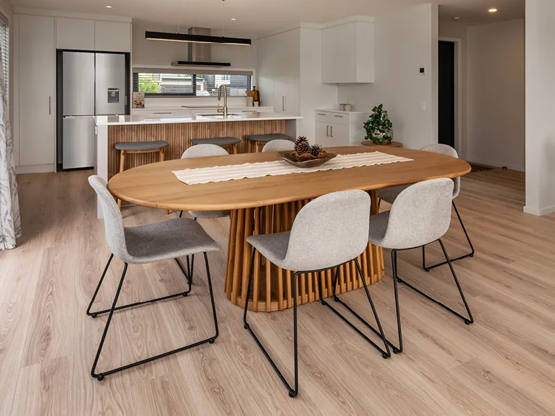 Dining area and kitchen in the Heart Foundation Home Lottery 162 three-bedroom house in Richmond, Nelson with wood table, modern chairs and island bench.