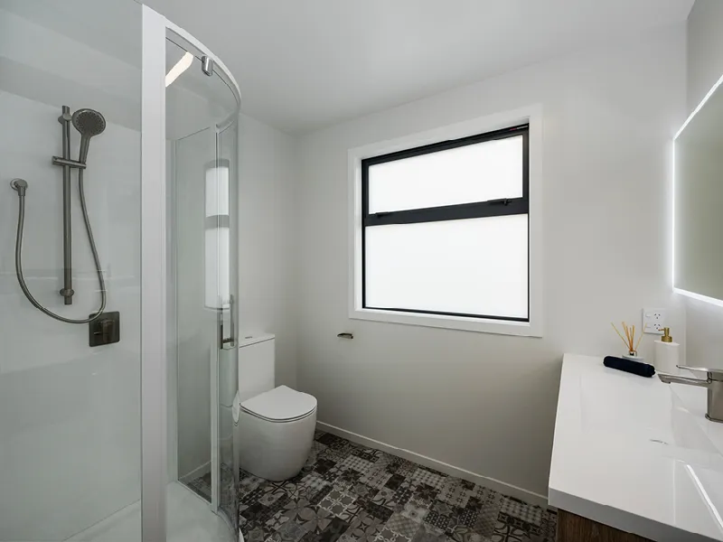 Modern bathroom in the Heart Foundation Home Lottery 162 three-bedroom house in Richmond, Nelson with tiled floor, glass shower and large vanity.