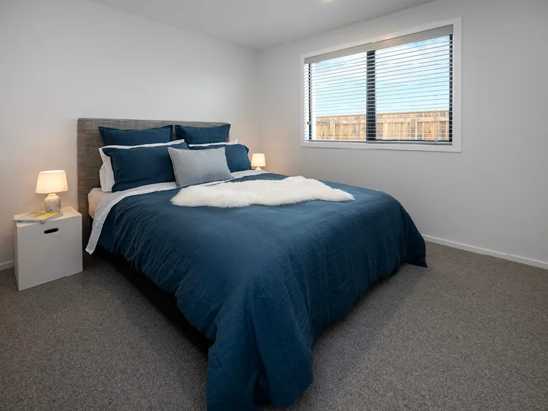 Second bedroom in the Heart Foundation Home Lottery 162 three-bedroom house in Richmond, Nelson with blue bedding, bedside lamps and large window.